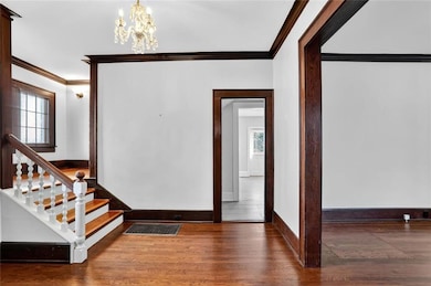 Foyer entrance featuring ornamental molding, dark wood-style flooring, a chandelier, and stairs