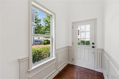 Doorway featuring healthy amount of natural light, a decorative wall, wainscoting, and dark wood-type flooring