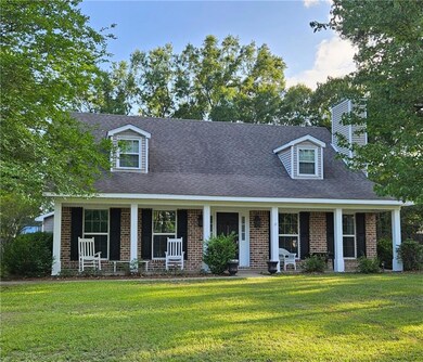 Cape cod home featuring covered porch, brick siding, a front yard, and roof with shingles