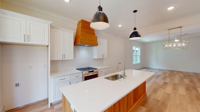 Kitchen featuring gas range, custom exhaust hood, a sink, light wood-style floors, and light countertops