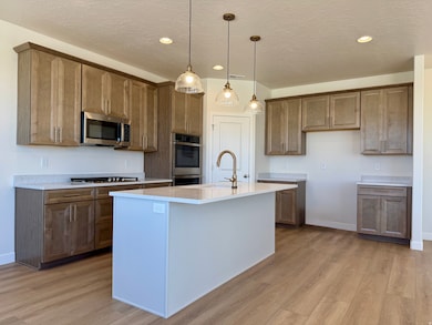 Kitchen with brown cabinetry, decorative light fixtures, light wood finished floors, a textured ceiling, and recessed lighting