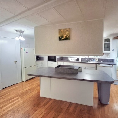 Kitchen with light wood finished floors, dark countertops, white appliances, and white cabinetry