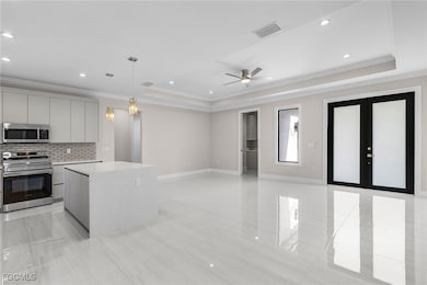 Kitchen featuring stainless steel appliances, backsplash, decorative light fixtures, a tray ceiling, and ornamental molding