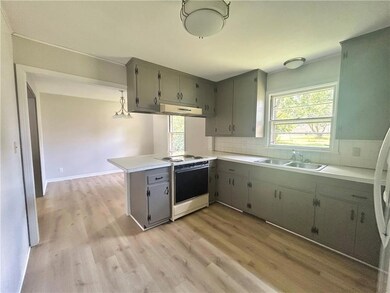 Kitchen with white range with electric stovetop, under cabinet range hood, a peninsula, decorative backsplash, and light wood finished floors