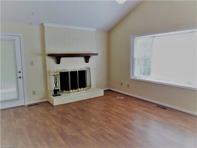 Open living room with vaulted ceilings, recent laminate flooring on ML, ceiling fan, large bay window, brick fireplace with a wide hearth and large wooden mantle, and gas logs!