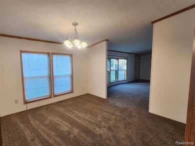 Spare room featuring crown molding, dark colored carpet, a textured ceiling, and a chandelier