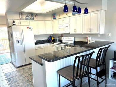 Kitchen featuring light tile patterned floors, white cabinetry, white appliances, a peninsula, and a kitchen breakfast bar