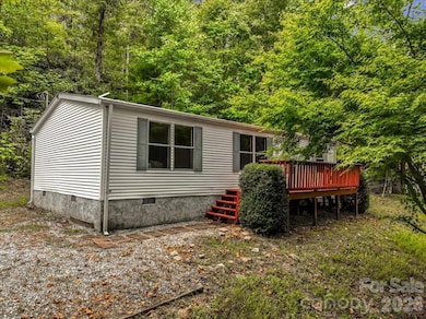 Front exterior of small home with white vinyl siding, red deck, and wooded setting. - 2271 Gouges Creek Rd, Spruce Pine, NC 28777