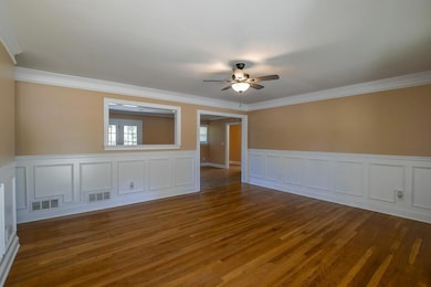Unfurnished room featuring wainscoting, dark wood-style flooring, ornamental molding, ceiling fan, and a decorative wall
