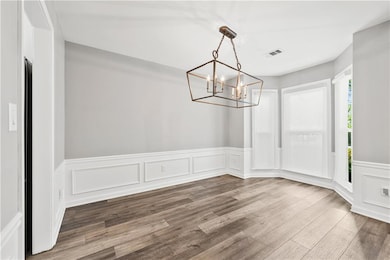 Unfurnished dining area with a chandelier, wood finished floors, a decorative wall, and wainscoting