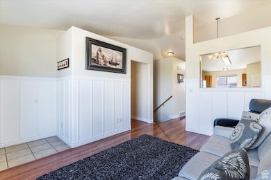 Living area with a decorative wall, light wood-style floors, a wainscoted wall, vaulted ceiling, and a chandelier