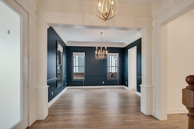 Unfurnished dining area with a chandelier, wood finished floors, ornamental molding, and baseboards