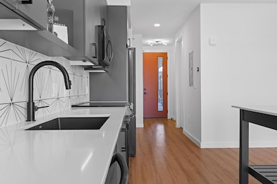 Kitchen featuring light wood-style floors, black appliances, tasteful backsplash, light stone countertops, and recessed lighting