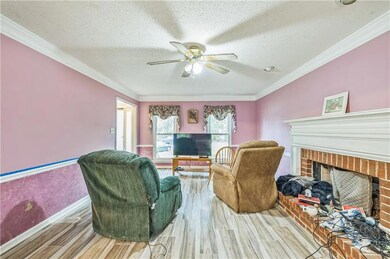 Living room featuring wood finished floors, a brick fireplace, a ceiling fan, a textured ceiling, and crown molding
