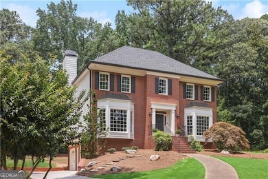 Colonial-style house featuring a chimney, brick siding, a front yard, concrete driveway, and a garage