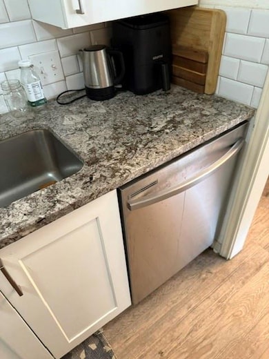 Kitchen view of dishwasher, white cabinetry, ston
