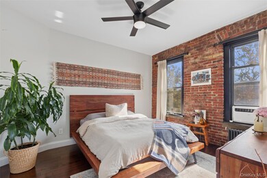 Bedroom with dark wood-type flooring, brick wall, and a ceiling fan