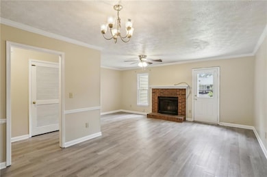 Unfurnished living room featuring ornamental molding, a textured ceiling, light wood-style floors, a brick fireplace, and ceiling fan