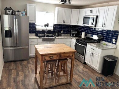 Kitchen with stainless steel appliances, white cabinets, light stone countertops, and decorative backsplash