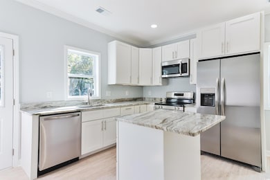 Kitchen with appliances with stainless steel finishes, a center island, white cabinetry, and sink