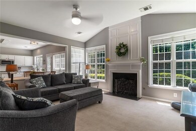 Living area featuring a fireplace with flush hearth, ceiling fan, light carpet, vaulted ceiling, and baseboards