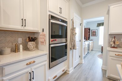 Kitchen with decorative backsplash, double oven, white cabinets, and crown molding