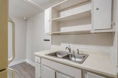 Kitchen featuring open shelves, light wood-style flooring, a textured ceiling, light countertops, and white cabinets