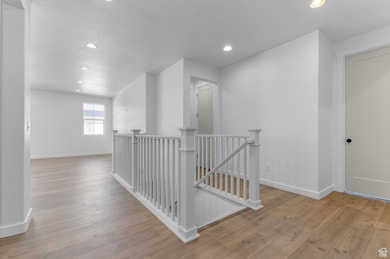 Hall with an upstairs landing, recessed lighting, light wood finished floors, and a textured ceiling