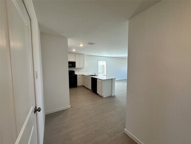 Kitchen with a peninsula, white cabinetry, light wood-style floors, black appliances, and light stone counters