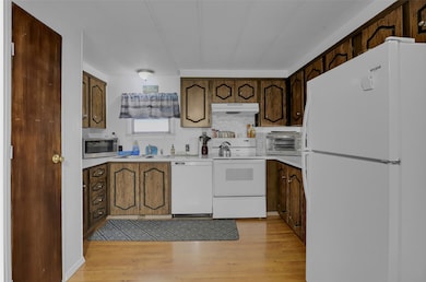 Kitchen featuring white appliances, light countertops, light wood finished floors, and under cabinet range hood