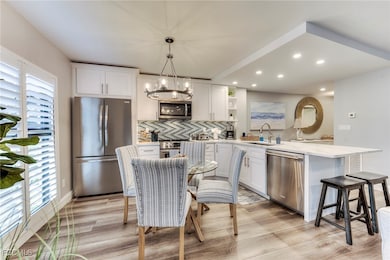 Kitchen with appliances with stainless steel finishes, a peninsula, open shelves, white cabinetry, and decorative light fixtures