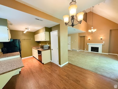 Kitchen featuring a chandelier, track lighting, white cabinetry, stainless steel microwave, and light wood-style flooring