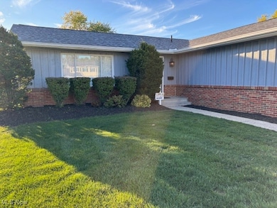 Entrance to property with a lawn, roof with shingles, board and batten siding, and brick siding