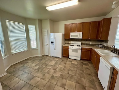 Kitchen featuring white appliances, light countertops, and brown cabinets