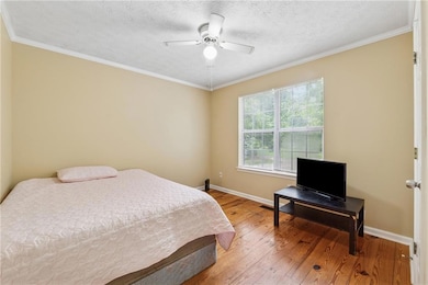 Bedroom with light wood-style flooring, ornamental molding, ceiling fan, and a textured ceiling