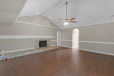 Unfurnished living room with dark wood-style flooring, a ceiling fan, a stone fireplace, and a wainscoted wall