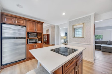 Kitchen with brown cabinetry, appliances with stainless steel finishes, light wood-style floors, a kitchen island, and wallpapered walls