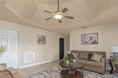Living area featuring a tray ceiling, ceiling fan, light wood-type flooring, and baseboards