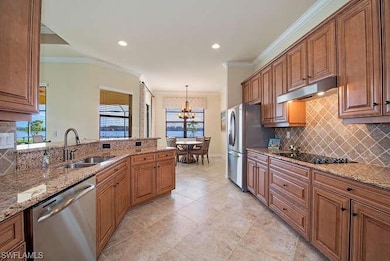 Kitchen featuring stainless steel appliances, a sink, under cabinet range hood, a chandelier, and backsplash