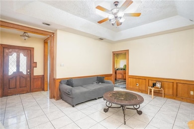 Living room with wainscoting, a textured ceiling, a raised ceiling, and a ceiling fan