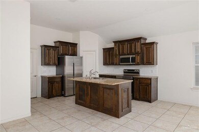 Kitchen with dark brown cabinets, tasteful backsplash, appliances with stainless steel finishes, light tile patterned floors, and light stone counters