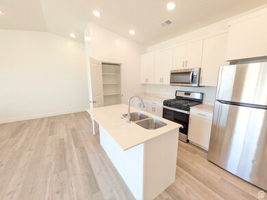 Kitchen featuring stainless steel appliances, vaulted ceiling, recessed lighting, an island with sink, and light wood-style flooring