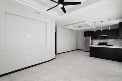 Kitchen with a raised ceiling, dark cabinetry, a peninsula, tasteful backsplash, and appliances with stainless steel finishes