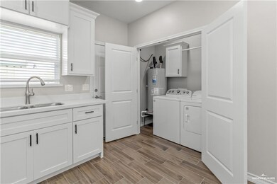 Washroom featuring independent washer and dryer, light wood-style flooring, a sink, electric water heater, and cabinet space