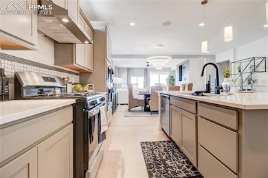 Kitchen with exhaust hood, appliances with stainless steel finishes, light countertops, a chandelier, and open floor plan