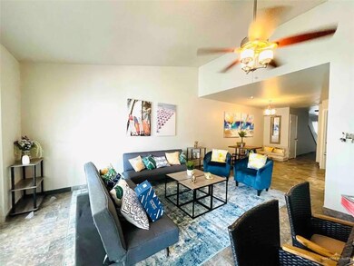 Tiled living room featuring ceiling fan with notable chandelier and vaulted ceiling