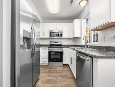 Kitchen with stainless steel appliances, dark countertops, dark wood-type flooring, and white cabinetry
