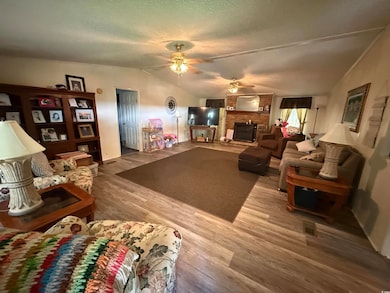 Living area featuring ceiling fan, lofted ceiling, a large fireplace, wood finished floors, and a textured ceiling