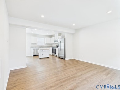 Kitchen featuring open floor plan, white cabinets, stainless steel appliances, light wood-style flooring, and light countertops