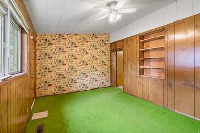 Carpeted empty room featuring wood walls, built in shelves, lofted ceiling, and a ceiling fan
